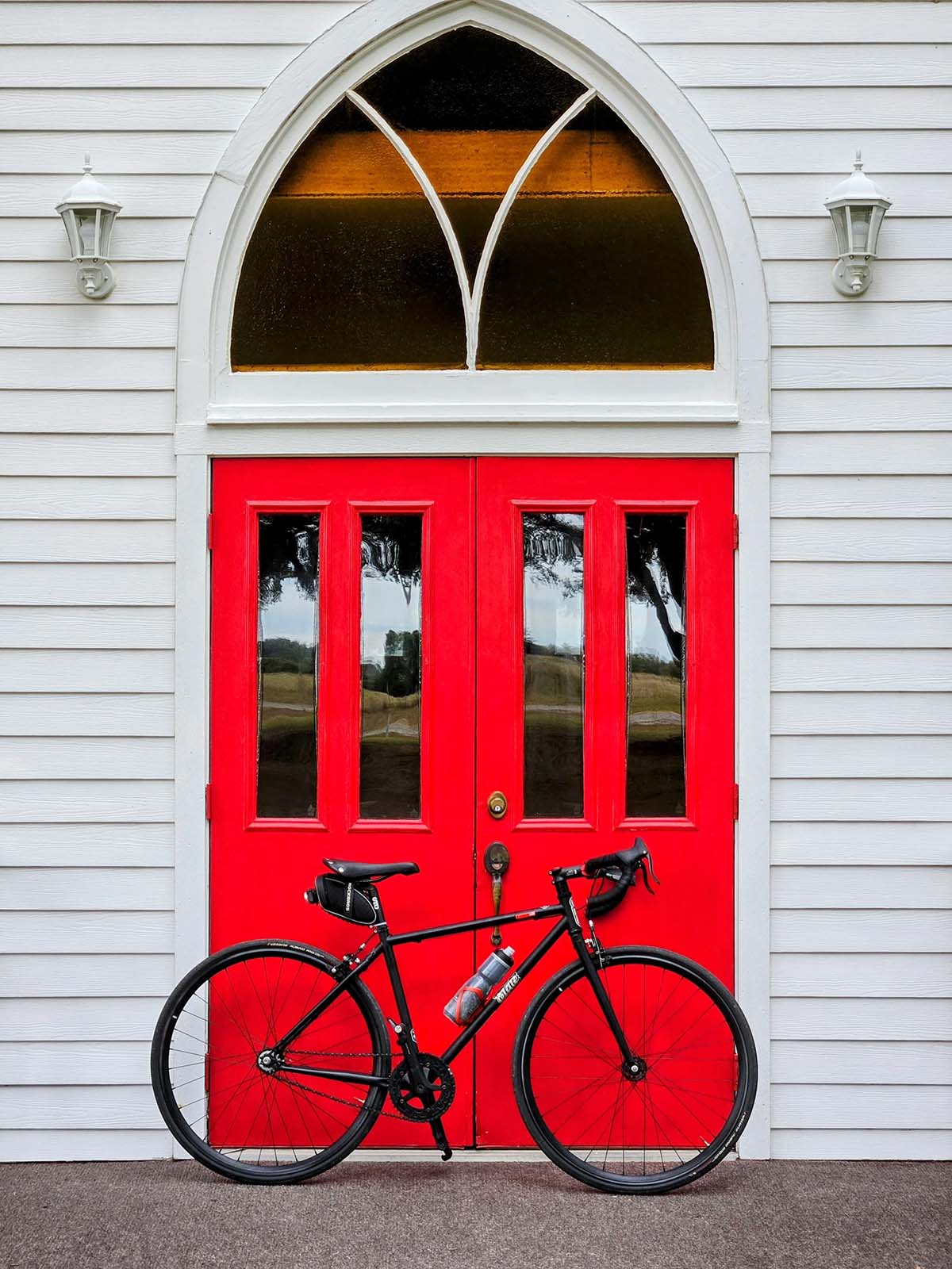 A road bike parked in front of the red chapel door