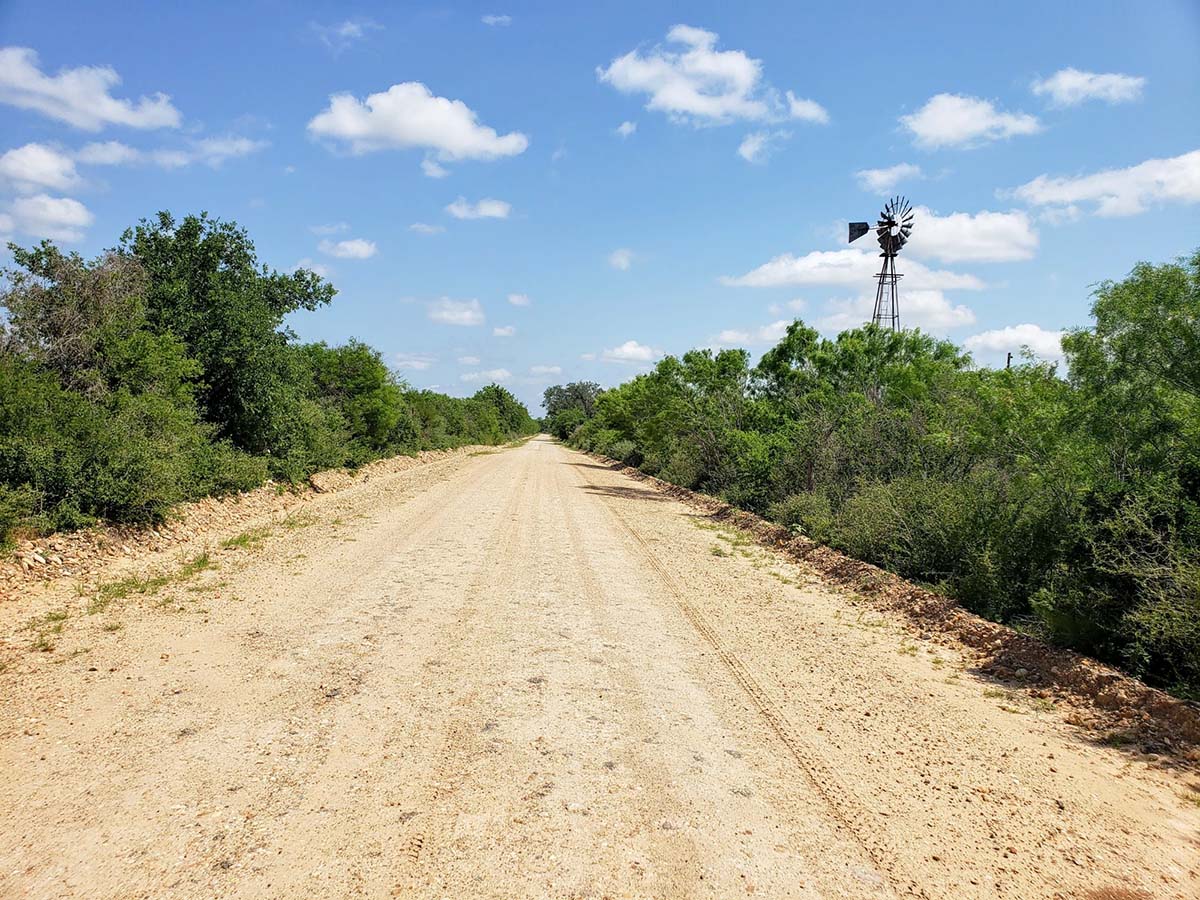 A beautiful gravel road in the Texas Hill country with a windmill in the distance